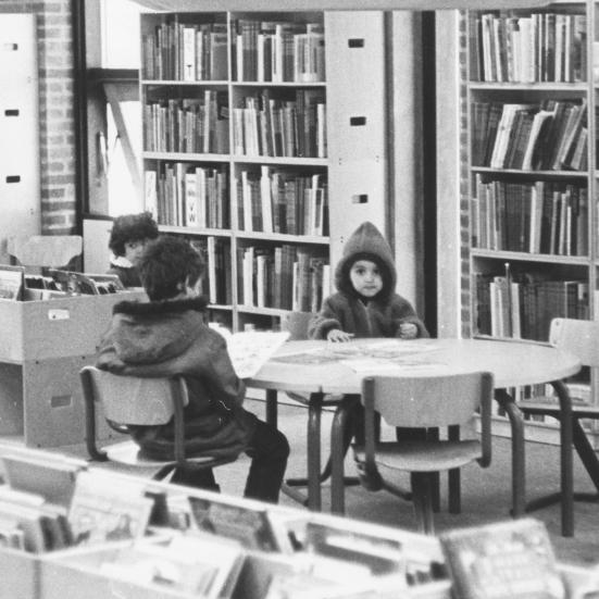 Tre små børn sidder ved et bord på biblioteket. Sort/hvid