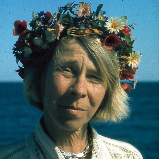 Portræt af Tove Jansson med en blomsterkrans på hovedet og havet som baggrunden