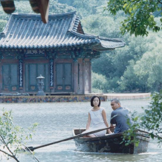 mand og kvinde i en båd på en sø, foran et koreansk hus