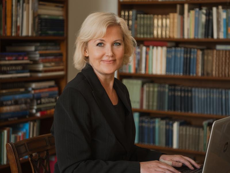 Portrætfoto af Anne-Matie Vedsø Olesen med bogreoler i baggrunden