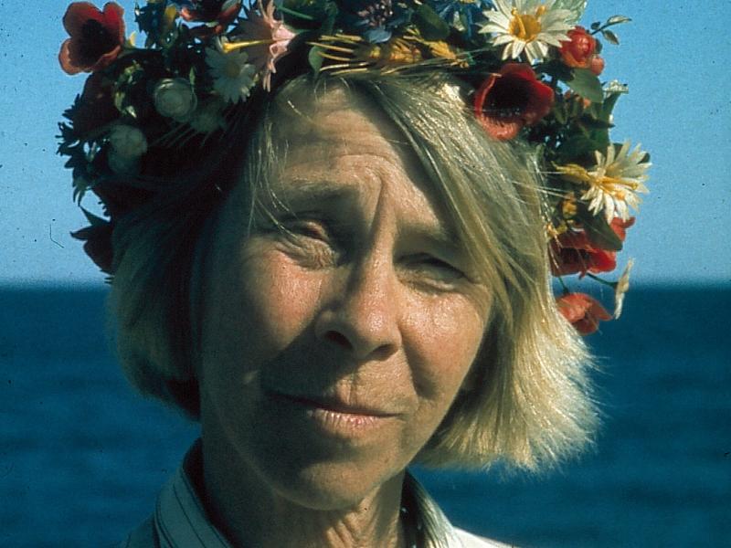 Portræt af Tove Jansson med en blomsterkrans på hovedet og havet som baggrunden