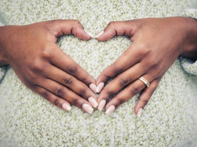 En kvinder laver et hjerte med sine hænder på sin gravide mave