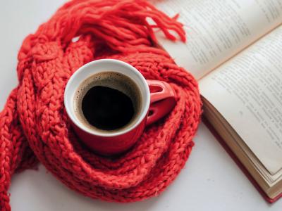 en kop kaffe med et halstørklæde omkring ved siden af en åben bog