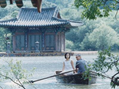 mand og kvinde i en båd på en sø, foran et koreansk hus