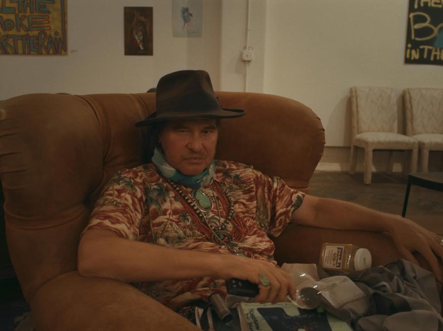 val kilmer sidder i en stol og ser på os