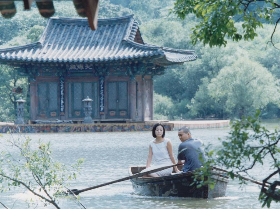 mand og kvinde i en båd på en sø, foran et koreansk hus