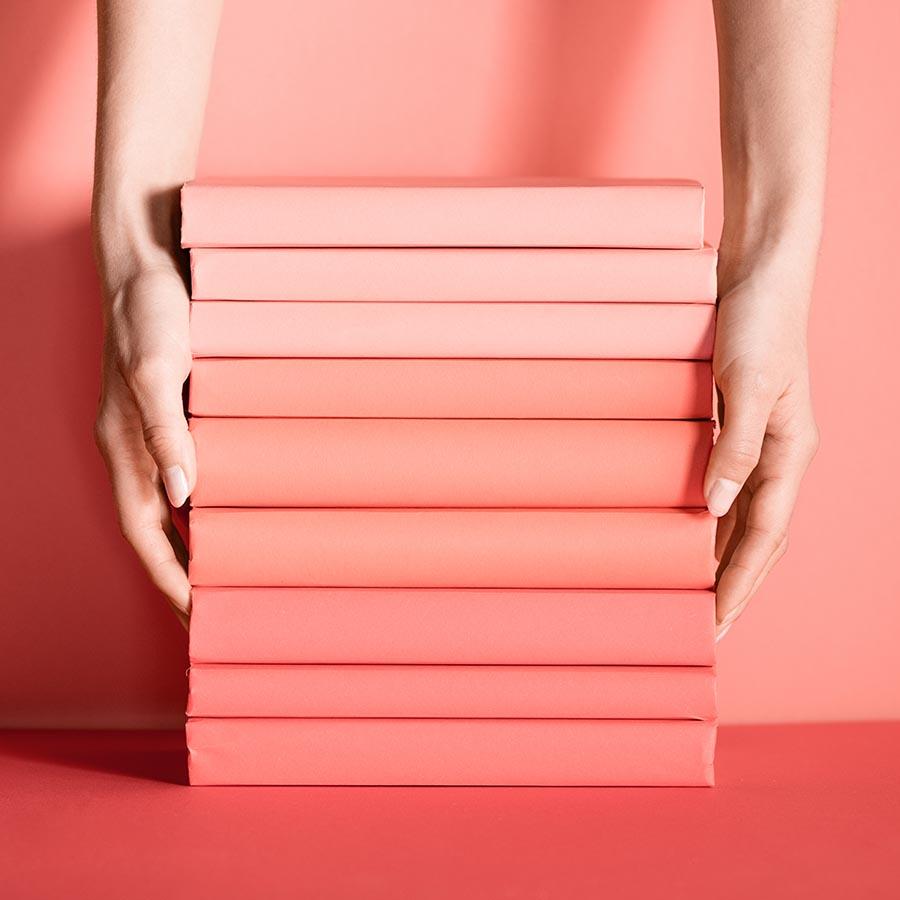Foto af en stabel bøger i rødlige nuancer, der bliver holdt af to hænder